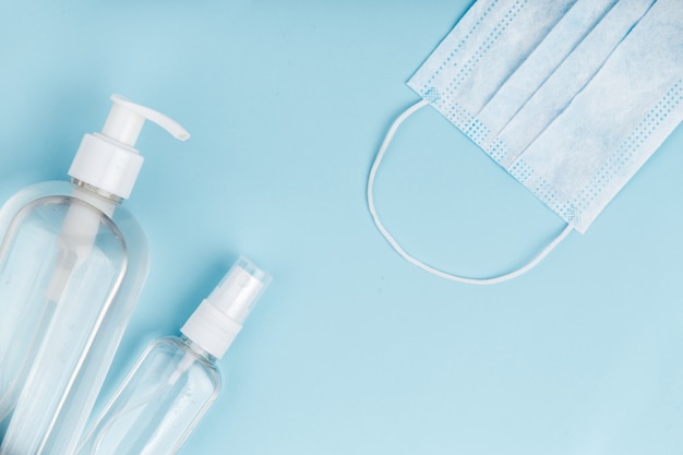 Hand sanitizer with medical mask on blue background.