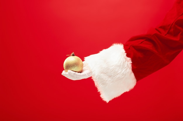 The hand of santa claus holding a Christmas decorations on red background. The season, winter, holiday, celebration, gift concept