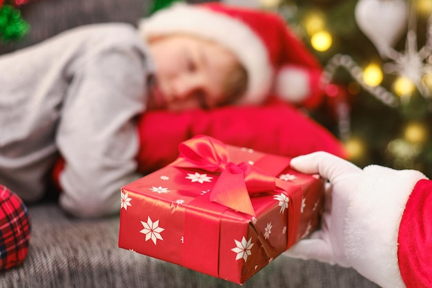 The hand of Santa Claus lays a Christmas gift to the boy