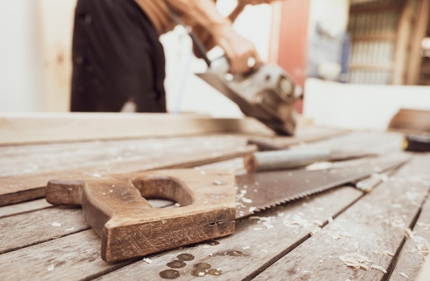 Sega a mano con manico in legno su falegname sfocato che lavora con pialla  elettrica per legno utensili da carpentiere