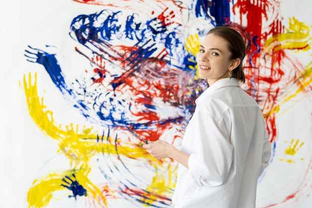 Hand schilderij kunst therapie ontspannen vrije tijd gelukkig lachende kunstenaar vrouw in wit overhemd op kleurrijke geel blauw rood abstract kunstwerk bevlekte muur achtergrond