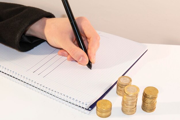 Hand schrijft een plan voor het berekenen van het inkomen van geldbesparingen in een notitieboek naast munten in stapels