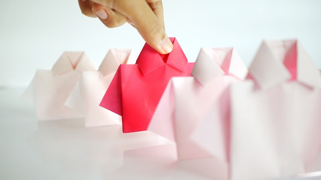 Hand selecting one Red among white origami shirt paper