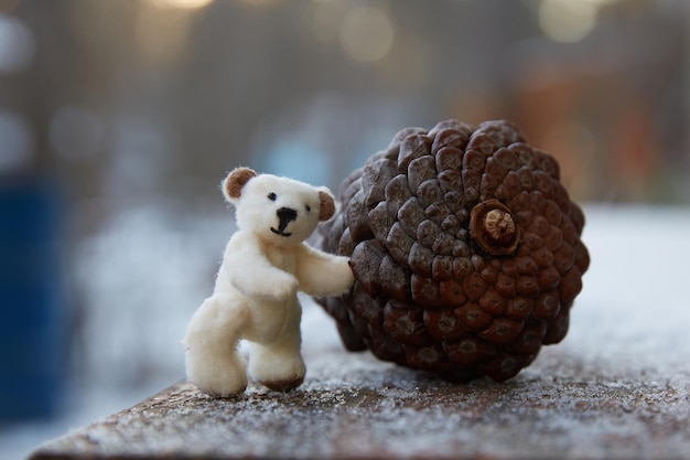 Hand-sewn micro-plush teddy bear rolls a large fir cone.