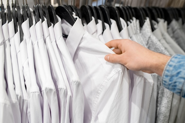 Рука покупателя выбирает белую рубашку в магазине одежды