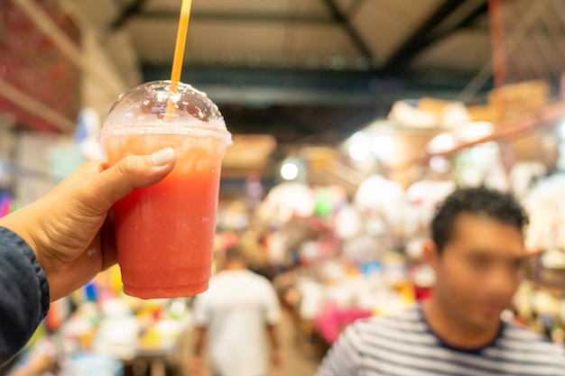 니카라과의 활기찬 시장 장면에서 플라스틱 유리에 치차 음료를 보여주는 손