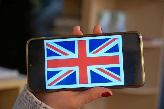더러운 화면에 영국 국기가 달린 스마트폰을 들고 있는 손
