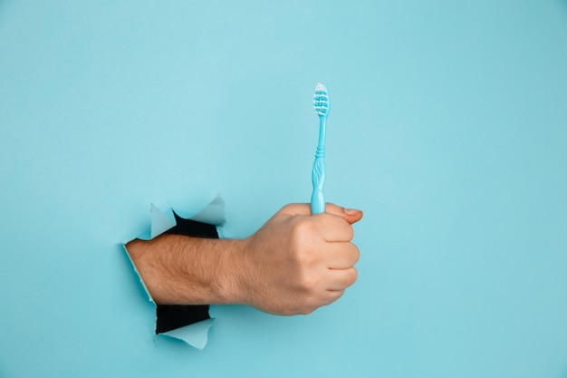 Mano che mostra uno spazzolino da denti da un buco strappato nel muro di carta. concetto di assistenza sanitaria