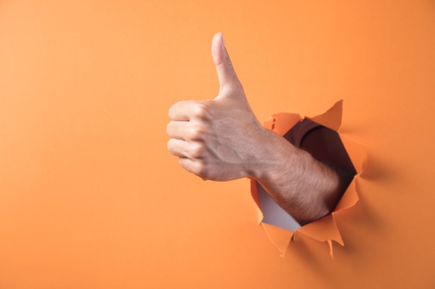 Hand shows thumbs up sign on orange background