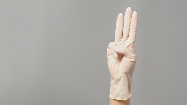 A hand sign of 3 fingers point upward meaning protest or three on grey background.Hand wear white medical glove.