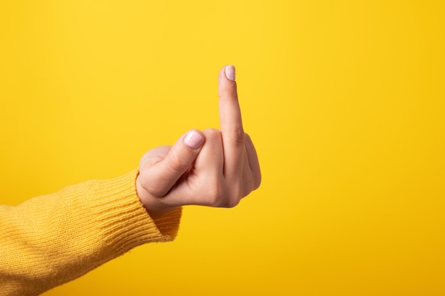 Hand sign showing middle finger in rude way meaning fuck off\
over yellow background