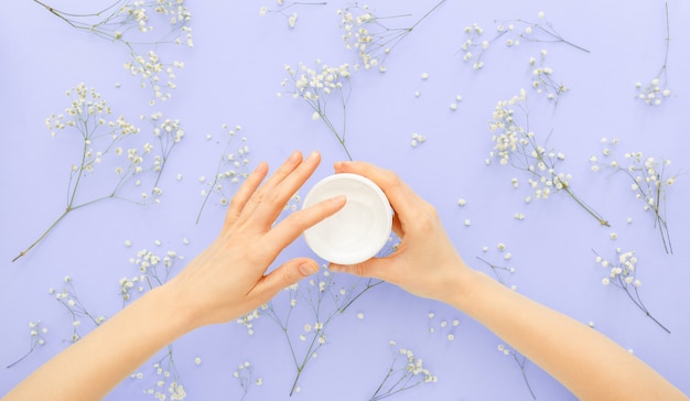 Hand Skin care cream in female hands applying organic natural cosmetics with flowers