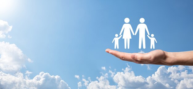 La mano sullo sfondo del cielo tiene l'icona della famiglia. concetto di assicurazione sanitaria e sulla vita. padre, madre, figlia e figlio.