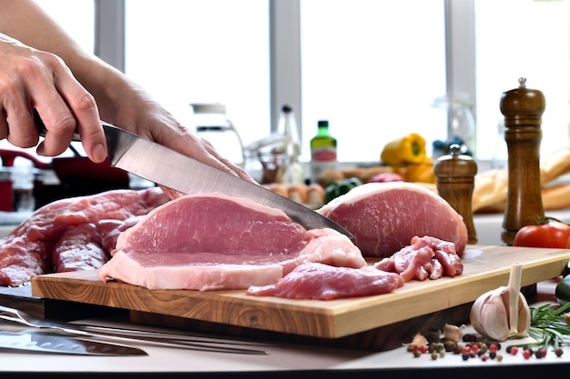 Hand slicing fresh raw pork meat on a cutting board in the kitchen