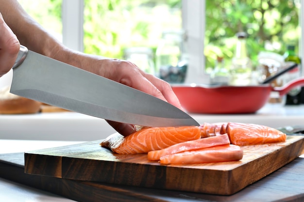 Фото Ручная нарезка стейков из свежего сырого филе лосося на разделочной доске на кухне