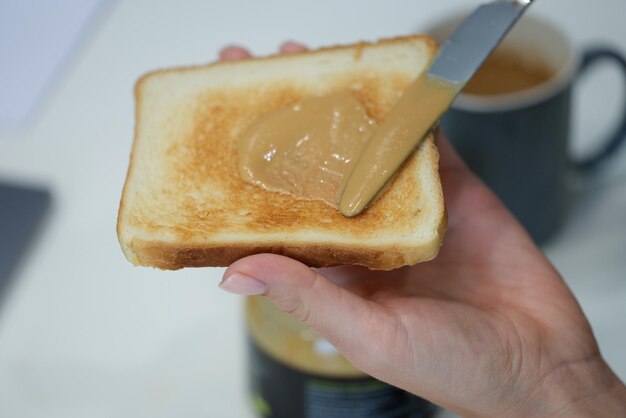 Hand smeert pindakaas op krokante toast close-up