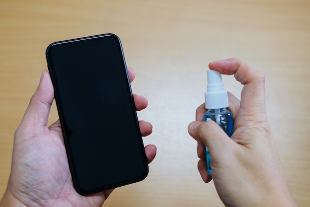 Photo hand spraying alcohol gel onto smartphone