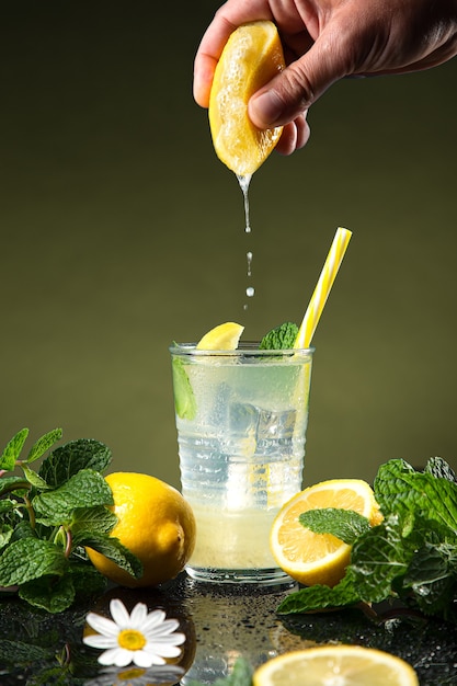 Hand squeezing lemon in lemonade, on dark background.