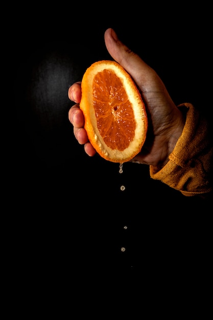 Hand squeezing orange on a black background