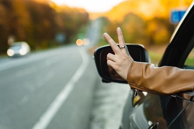秋の季節に道路の横に駐車した車の窓から手を伸ばし,平和のサインを示します