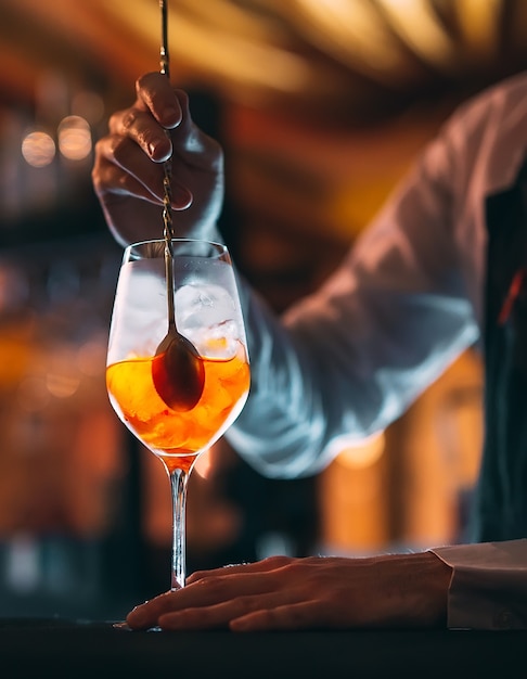 Mano mescolando cocktail estivo con un cucchiaio sul bancone del bar