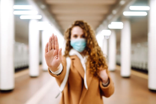 Hand stopbord. Vrouw met een steriel medisch masker op haar gezicht, toont stophandengebaar voor stop uitbraak van coronavirus op metrostation.