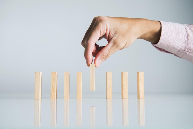 Hand stopping wooden domino business crisis effect or risk\
protection concept