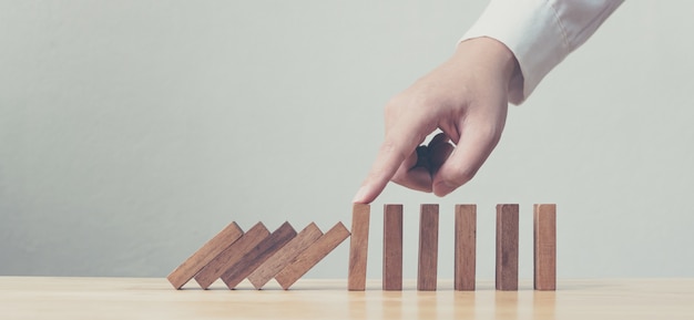 Hand stopping wooden domino business crisis effect