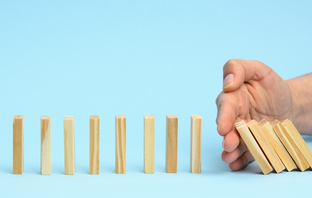 Hand stops the fall of wooden bars on a blue surface