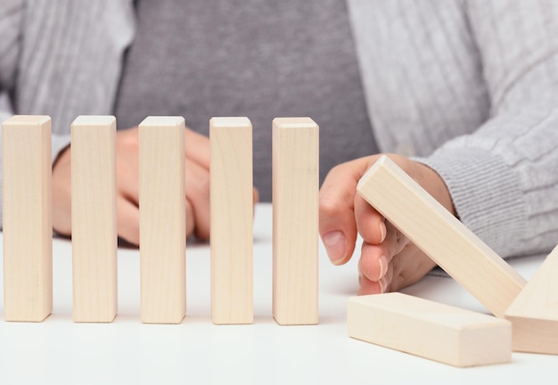 Hand stops the fall of wooden blocks on a white background.
concept of a strong and courageous personality capable of
withstanding unequal difficulties. strong business, control of the
situation