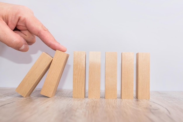 Photo hand stops and protects the fall of a wooden block, risk protection concept. domino effect.