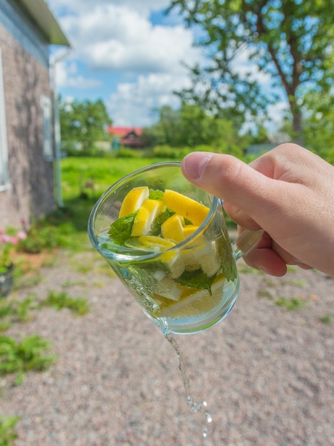 В руке летний напиток с лимоном и мятой, он течет из кружки.