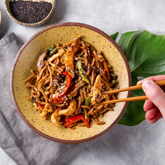 Hand takes chopsticks asian buckwheat soba noodles with vegetables mushrooms and chicken square