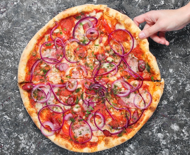 La mano prende un pezzo di pizza fatta in casa su sfondo grigio cemento