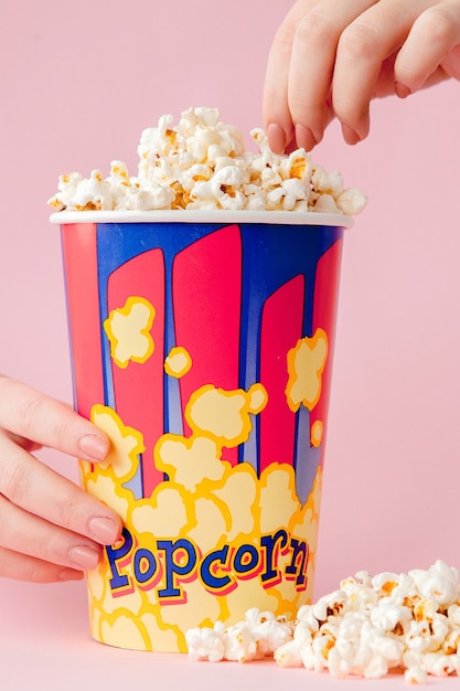 Hand takes a popcorn from a paper cup on pink.