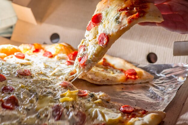 Foto la mano prende una fetta di pizza fresca tirando il formaggio fuso fuori dalla scatola consegna del cibo