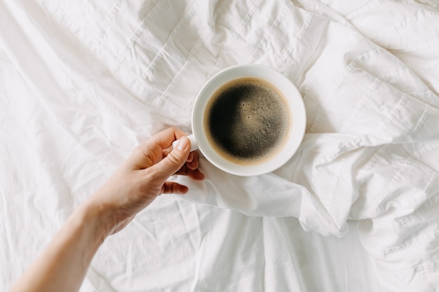 Hand taking a cup of coffee on white bed sheet Breakfast in bed concept