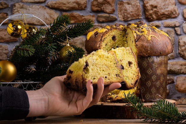 A hand taking a cut piece of traditional italian christmas cake panettone with festive decoration on