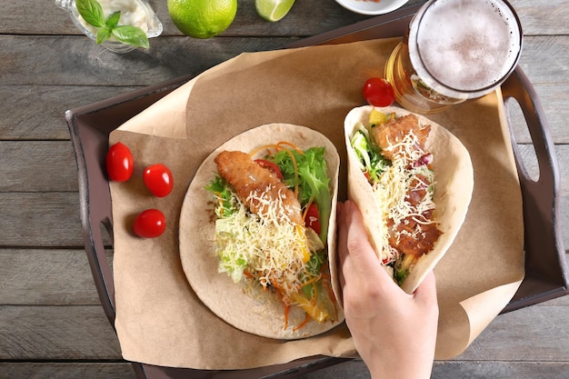 Foto mano prendendo deliziosi tacos di pesce serviti sul vassoio sul tavolo di legno