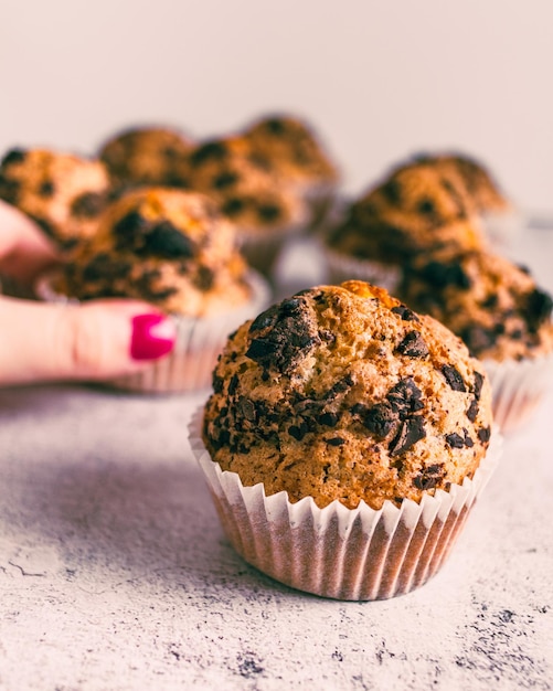 Hand taking homemade muffin with chocolate chips on white background.