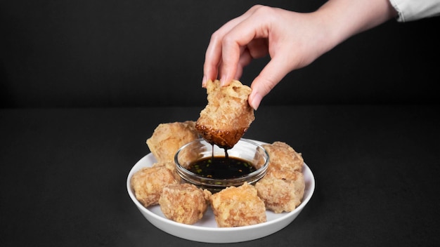 Hand taking one fried tofu fritters from a chilli soybean sauce