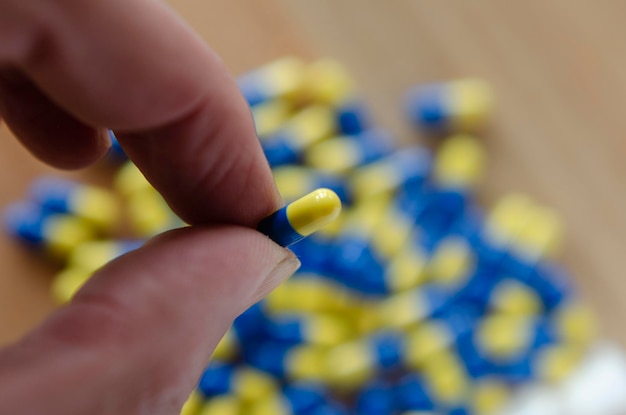 Photo hand taking pill in capsule with fingers with background of many drugs from the pharmaceutical industry