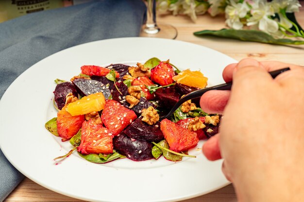 올리브 오일을 곁들인 맛있는 비트 뿌리 오렌지 호두와 아루굴라 샐러드의 일부를 손으로 가져갑니다.