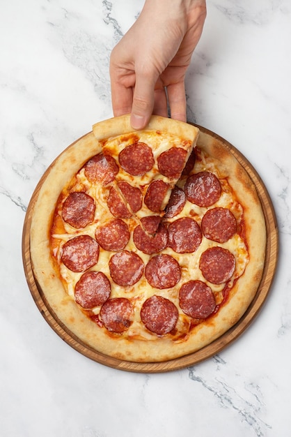 Hand taking a slice of pepperoni pizza on a gray background