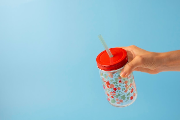 Photo hand taking a transparent glass with flowers and a drinking straw on a blue background copy space