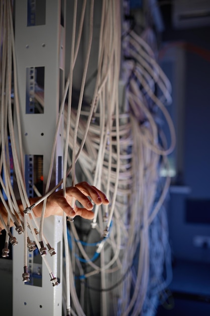 ワイヤーに絡まった手。多くのケーブルが機能し、最新のデータ センター コンセプトのサーバー ルームでのインターネット接続に問題があります。