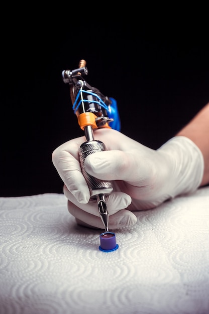 Hand of a tattoo master with a tattoo gun. Hand of a tattoo specialist and a tattoo gun.