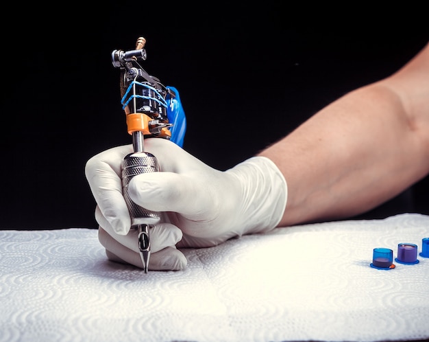 Hand of a tattooer with a tattoo gun.