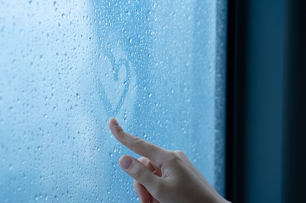 Hand tekenen van een hart op een mistig raam tijdens de regen