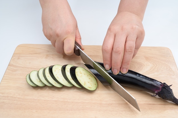 A hand that cuts eggplant on a cutting board.